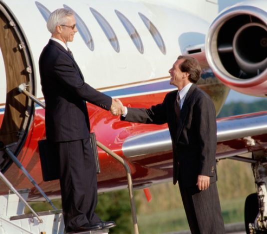 Two businessmen shaking hands near an airplane